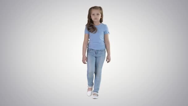 Niña en jeans y camiseta azul caminando sobre fondo degradado. — Vídeos de Stock