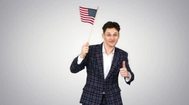 Resmi takım elbiseli genç adam arka planda Amerikan bayrağıyla komik bir şekilde dans ediyor..