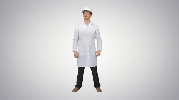 Scientist Engineer dalam jubah putih, helm keselamatan dan kacamata Membuat gerakan lucu dengan matanya pada akhirnya pada latar belakang gradien. — Stok Video