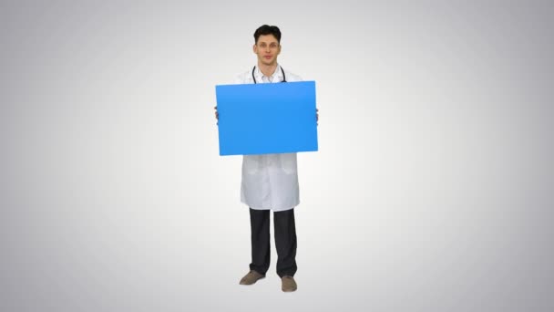 Feliz sorrindo médico masculino mostrando placa em branco e dançando em fundo gradiente. — Vídeo de Stock