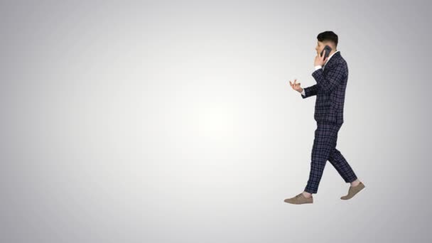 Joven hombre emocional enojado en traje formal hablando por teléfono y bailando después en el fondo gradiente. — Vídeo de stock