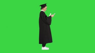 Diploması olan mutlu bir bayan mezun ve yeşil ekranlı Chroma Key 'de telefonuyla mesajlaşıyor..