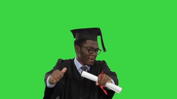 Izgalmas afro-amerikai férfi diák ballagási köntösben boldogan táncol a diplomájával egy zöld vásznon, Chroma Key. — Stock videók