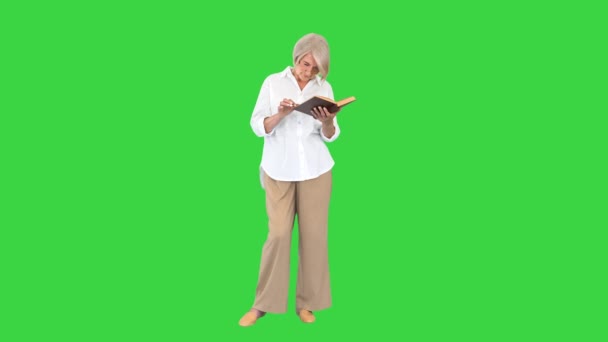 Старушка стоит и читает книгу на зеленом экране, Chroma Key. — стоковое видео