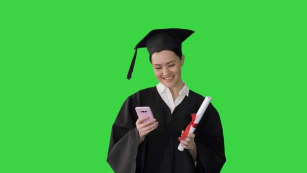Feliz graduada con diploma y mensajes de texto en su teléfono en una pantalla verde, Chroma Key. — Vídeo de stock