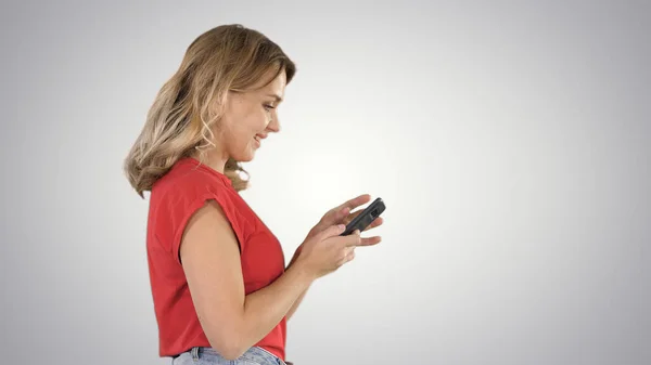 Счастливая симпатичная молодая женщина играет в игры по мобильному телефону на заднем плане. — стоковое фото
