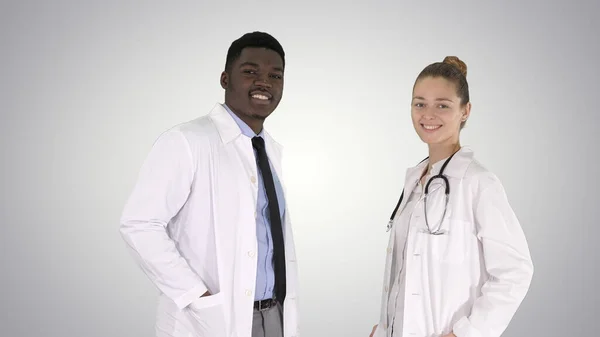 Due medici caucasici e afro-americani sorridenti in piedi guardando in macchina fotografica su sfondo sfumato. — Foto Stock