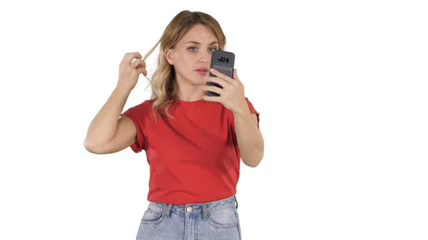 Una bella giovane donna raddrizza i capelli guardando nel cellulare su sfondo bianco. — Foto Stock