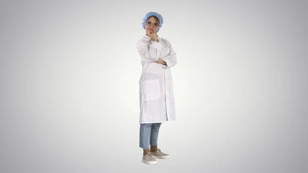 Sorridente fiducioso giovane donna medico in piedi con le braccia incrociate su sfondo sfumato. — Foto Stock