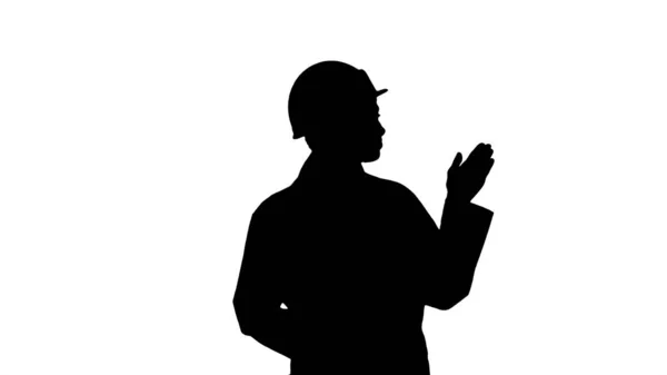Silhouette Ältere Ingenieurin mit Hut, die beim Gehen mit den Händen auf das Produkt oder den Text hinweist. — Stockfoto