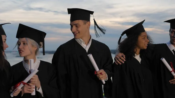 Gemengde races gelukkige studenten in klassieke afstuderen mantels en aca — Stockfoto