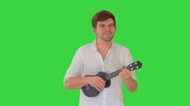 Yeşil Ekran 'da yürürken ukulele çalan genç adam, Chroma Key.