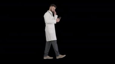 Beyaz üniformalı bir erkek doktor Alpha Channel 'da yürüyor ve akıllı telefon kullanıyor.