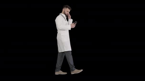 Médico varón en uniforme médico blanco caminando y usando smartphone, Alpha Channel — Vídeos de Stock