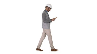 Genç mimar beyaz arkaplanda yürürken ders kitabı ya da not defteri okuyor.