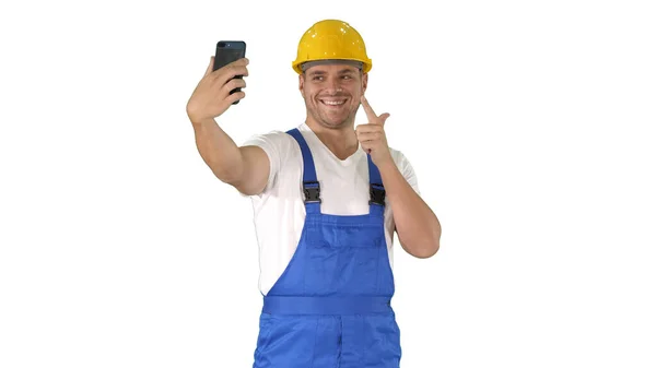 Lachende knappe jonge bouwer maken selfie met mobiele telefoon op witte achtergrond. — Stockfoto