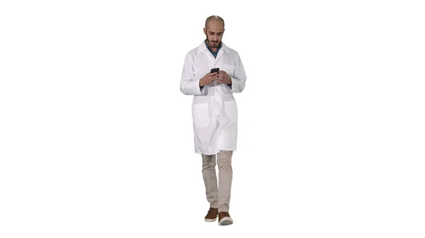 Male arab doctor texting message on the phone while walking on white background. — Stock Photo, Image