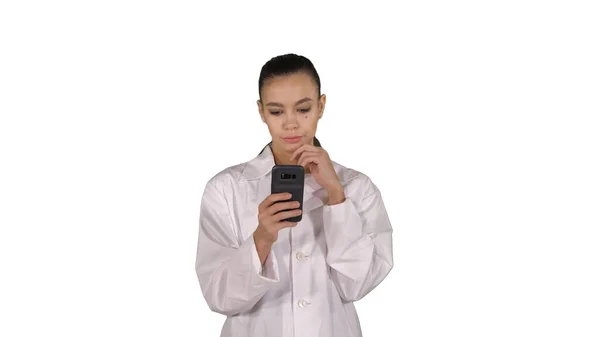 Vrolijke schattige jonge vrouw arts typen tekst op telefoon tijdens het lopen op witte achtergrond. — Stockfoto