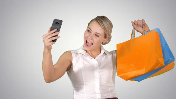Venta, consumismo, tecnología y concepto de personas - mujer joven feliz con smartphone y bolsas de compras tomando selfie en el fondo gradiente. —  Fotos de Stock