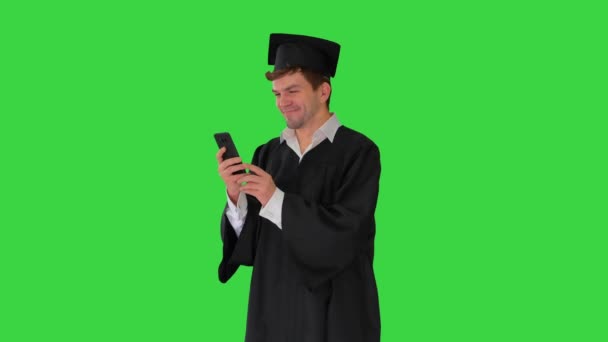 身着毕业礼服的男生笑着，在绿色屏幕上的手机上挂着"铬钥匙"的留声机. — 图库视频影像