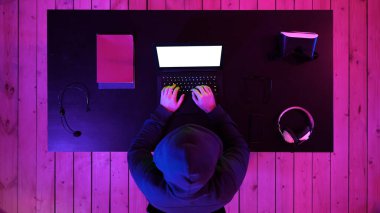 Kapüşonlu bilgisayar korsanı karanlık stüdyoda dizüstü bilgisayar kullanıyor. Beyaz Görünüm.