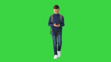 Sırt çantalı öğrenci yeşil ekranda yürürken cep telefonu kullanıyor, Chroma Key.
