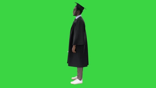 Африканский американец в выпускном халате, сложив руки с дипломом, с большой улыбкой смотрит на зеленый экран, Chroma Key. — стоковое видео