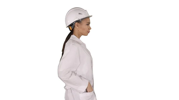 Mujer en bata blanca poniéndose un sombrero duro mientras camina sobre fondo blanco. —  Fotos de Stock