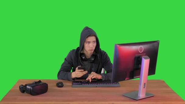 Hacker con cappuccio utilizzando laptop e smartphone su uno schermo verde, Chroma Key. — Video Stock