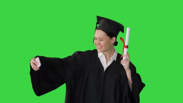 Feliz mujer graduada sosteniendo diploma y haciendo selfie en su teléfono en una pantalla verde, Chroma Key. — Vídeos de Stock