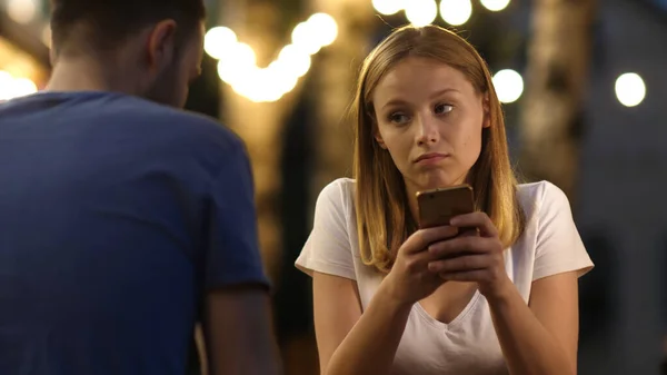 Znudzona nastolatka na randce z telefonem. Para spędza czas przewijając strony internetowe na telefonach. — Zdjęcie stockowe