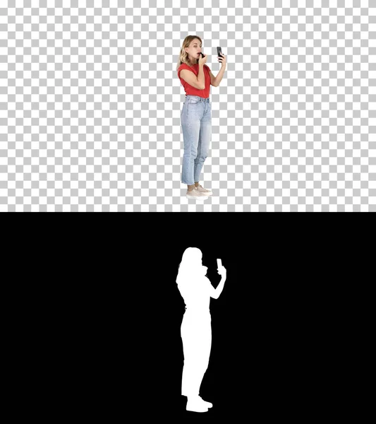 Egy nő rúzsozza magát és belenéz a telefonjába, Alpha Channel. — Stock Fotó