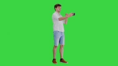 Günlük beyaz gömlekli genç adam yeşil ekranda, Chroma Key 'de telefonuyla selfie çekiyor..