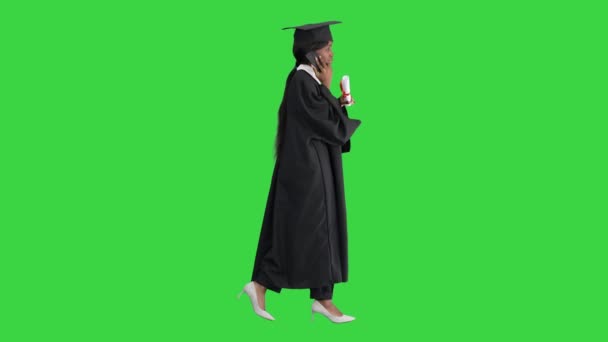 Afro-Amerikaanse vrouwelijke student in afstuderen badjas praten aan de telefoon tijdens het lopen op een groen scherm, Chroma Key. — Stockvideo