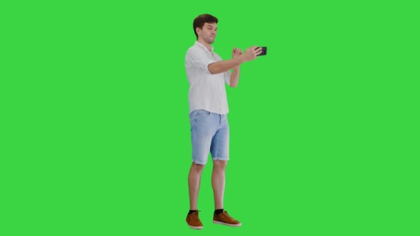 Jeune homme en chemise blanche décontractée prenant selfies sur son téléphone sur un écran vert, Chroma Key. — Video