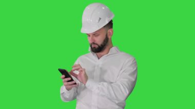 Beyaz gömlekli ve güvenlik mühendisi şapkalı akıllı mühendis yeşil ekranda akıllı telefon kullanıyor, Chroma Key.