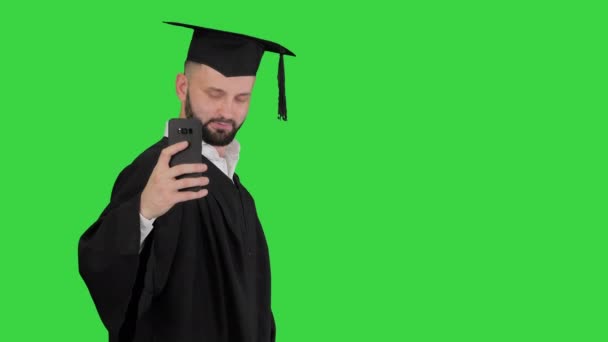 卒業ローブを身に着けている男歩くと緑の画面上の卒業証書で自撮り,クロマキー. — ストック動画