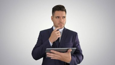 Genç işadamı tablete bakıyor ve gradyan arkaplan üzerinde düşünüyor.