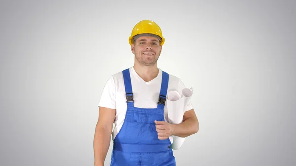 Trabajador de la construcción caminando con impresiones azules y sonriendo a la cámara sobre fondo degradado. — Foto de Stock