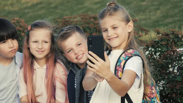 Cuatro niños están sentados en un banco y tratando de hacer selfie. — Foto de Stock