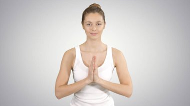 Yoga yapan, namaste yapan, spor yapan, arka planda beyaz tişört giyen genç yogi kadın..