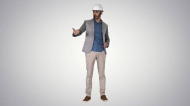 Mimar adam miğfer ve kafa setinde kamerayla konuşuyor ve grafiksel arkaplanda bazı objeler üzerinde jestler yapıyor..