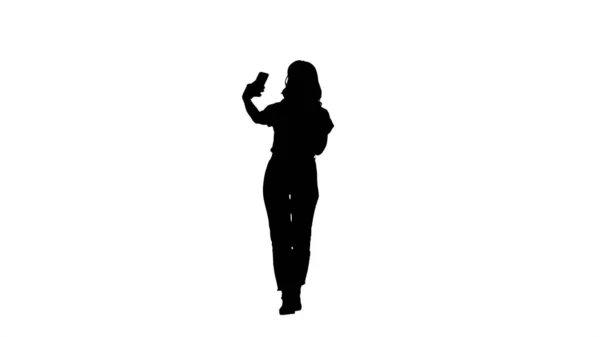 Silhouette Linda chica sexy con el pelo rubio rizado caminando y haciendo selfie. — Foto de Stock