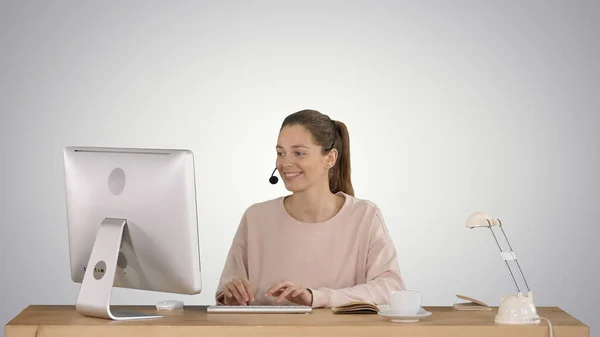 Bella giovane donna casual che indossa auricolare lavorando sul computer su sfondo gradiente. — Foto Stock