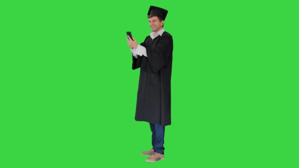 Étudiant souriant en robe de remise des diplômes montrant campus via appel vidéo sur son téléphone sur un écran vert, Chroma Key. — Video