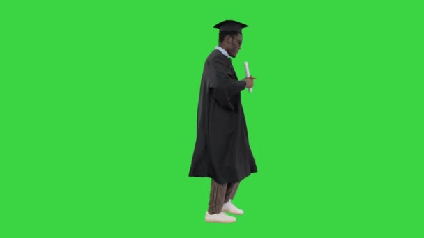 Eccitato studente afroamericano maschio in vestaglia laurea ballare con il suo diploma mentre cammina su uno schermo verde, Chroma Key. — Video Stock
