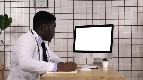 Ο γιατρός κρατάει σημειώσεις ψάχνοντας πληροφορίες στον υπολογιστή του. Λευκή οθόνη. — Φωτογραφία Αρχείου