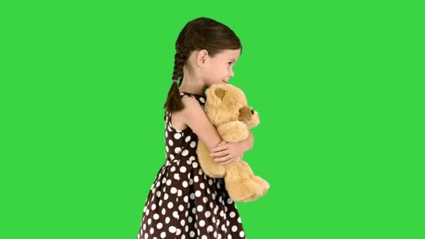 Kleines Mädchen im gepunkteten Kleid umarmt großen Teddybär beim Gehen und schaut in die Kamera auf einem Green Screen, Chroma Key. — Stockvideo