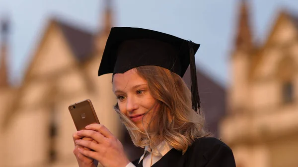 Young cute student graduate texting message on her phone.