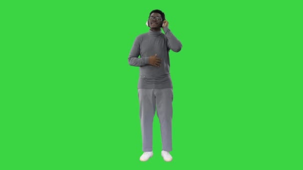 Sorrindo afro-americano em fones de ouvido e movendo-se para o ritmo da música em uma tela verde, Chroma Key. — Vídeo de Stock